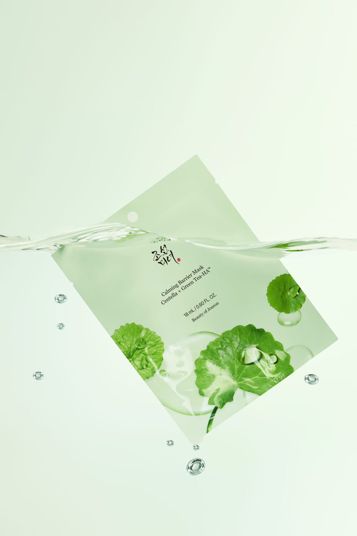A light green skincare packet with green leaf illustrations and Korean text, floating diagonally in clear water with bubbles and a wave line across the middle.
