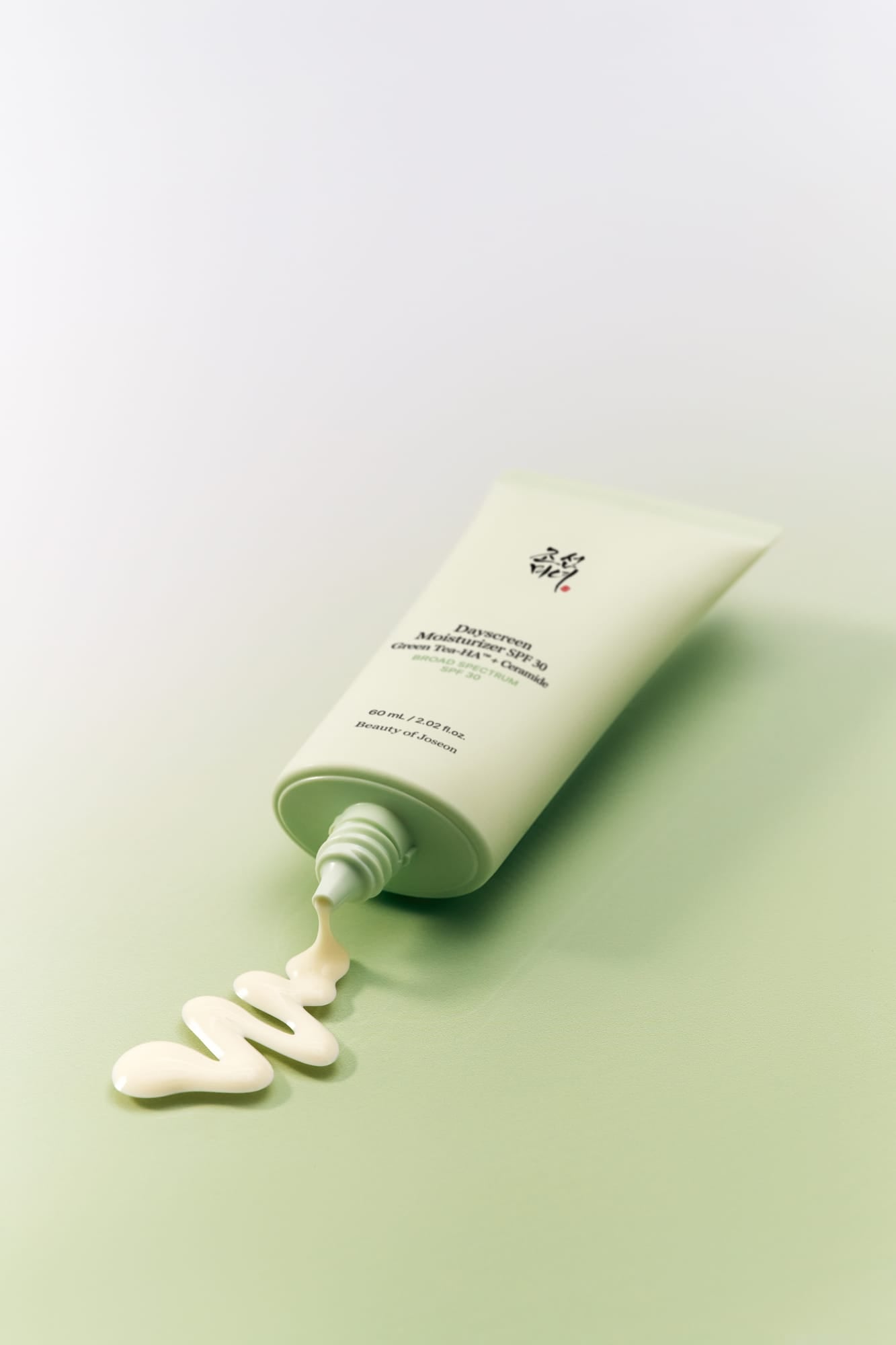 Green skincare product with white cream being squeezed out on a light green background